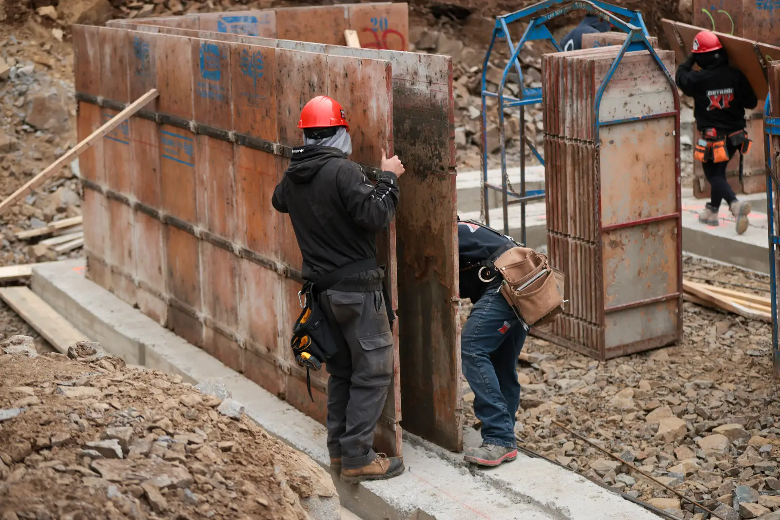 Mur de fondation coffré, deux travailleurs à l'ouvrage.