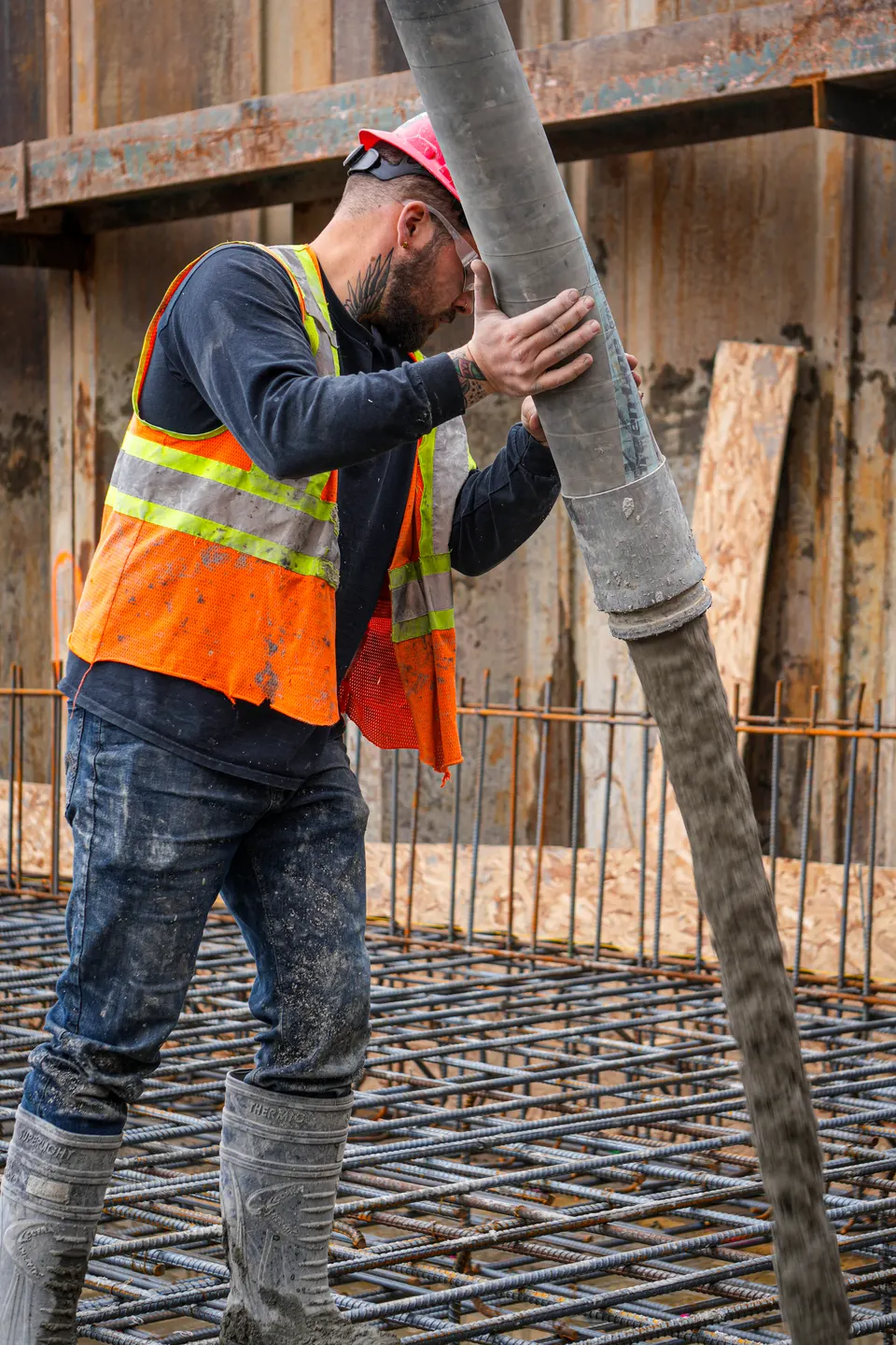 Travailleur guidant le tuyau de la pompe pendant que le béton se déverse sur l'armature.