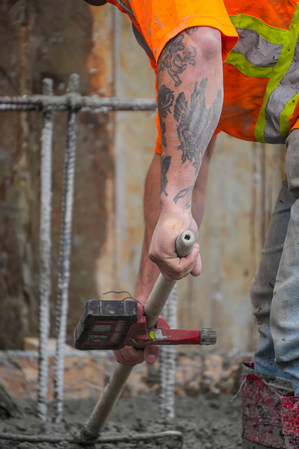 Avant-bras tatoué tenant un vibrateur à béton au-dessus des barres d'armature.