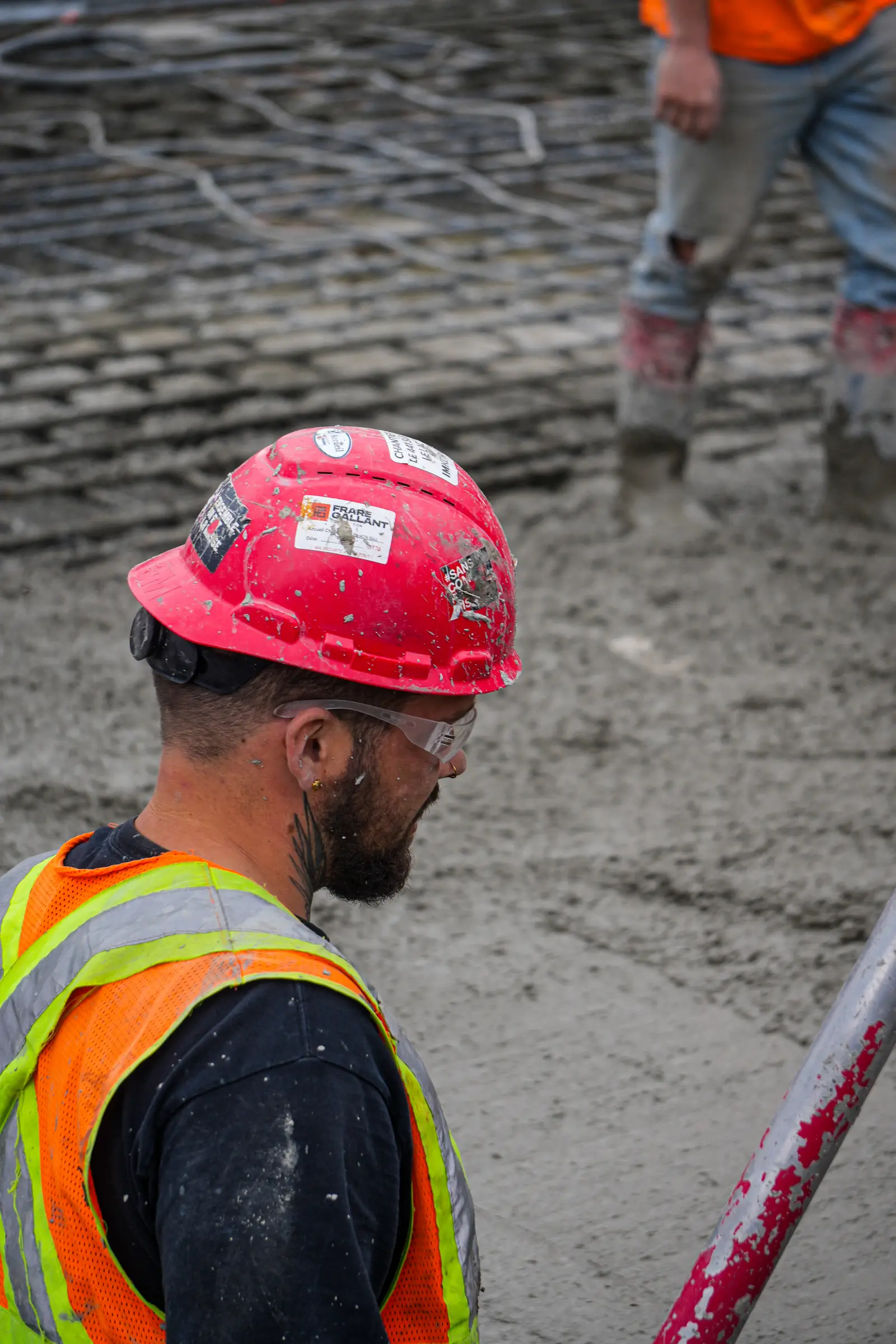 Profile portrait of a worker, red hard hat covered in stickers and a safety vest.