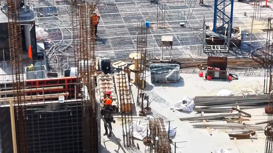 Chantier urbain vu d'en haut : coffrages de murs PERI rouges et noirs en place, armatures de colonnes et grue à tour sur la dalle.