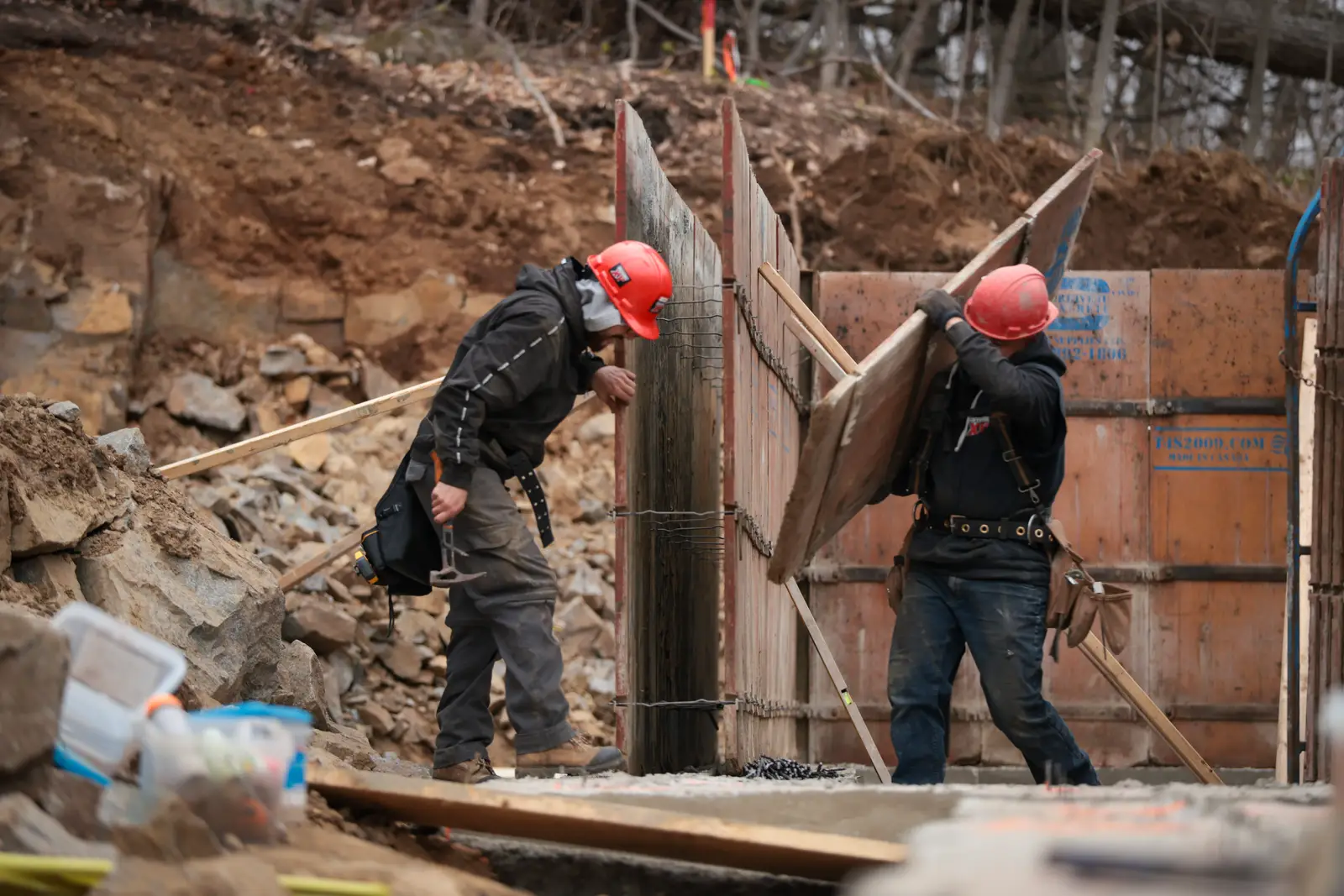 Deux travailleurs assemblent un coffrage au fond d'une excavation.