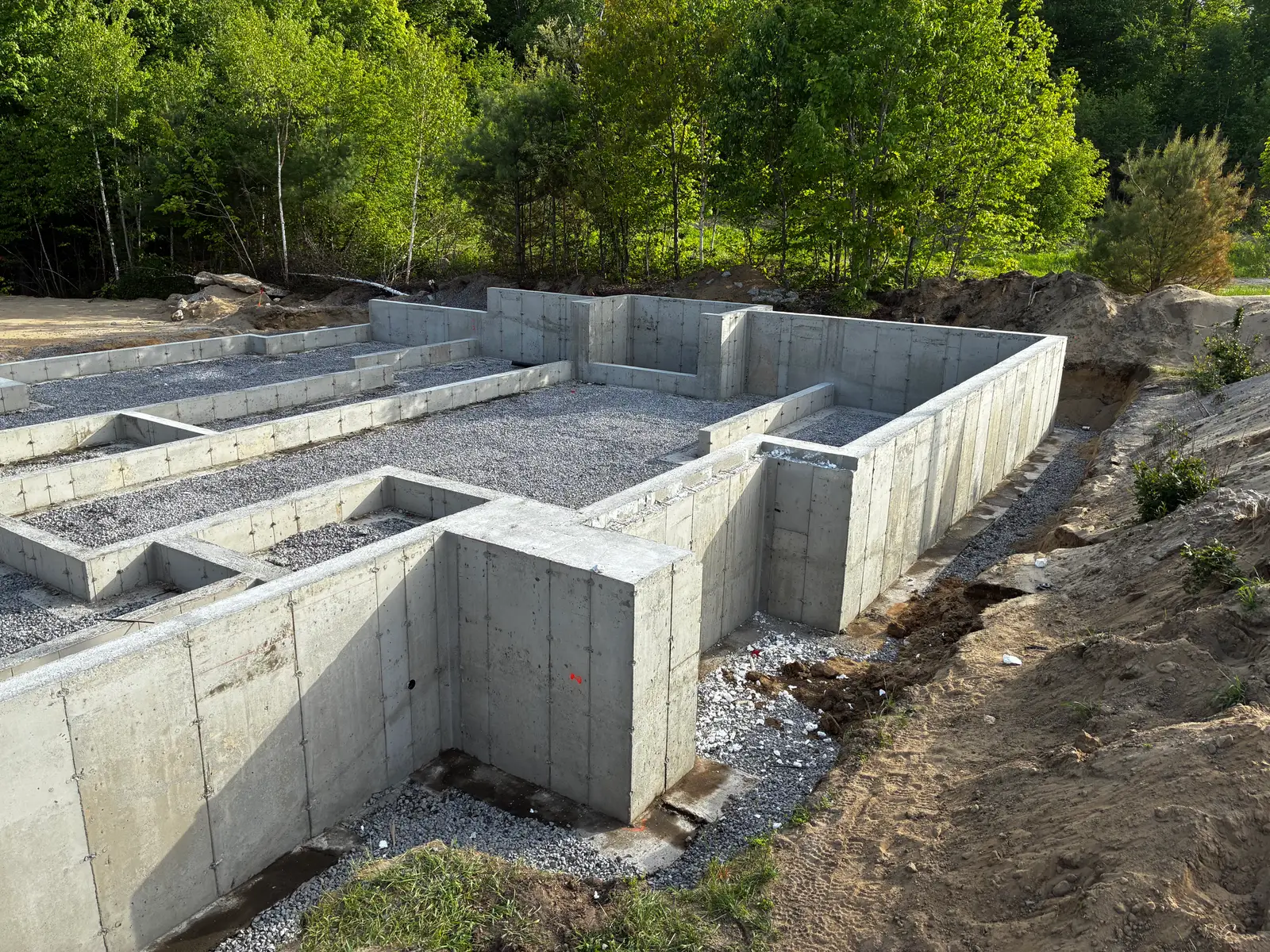 Fondation résidentielle décoffrée au complet, chaque pièce du sous-sol délimitée par ses murs, fond de pierre concassée nivelé, forêt à l'arrière.