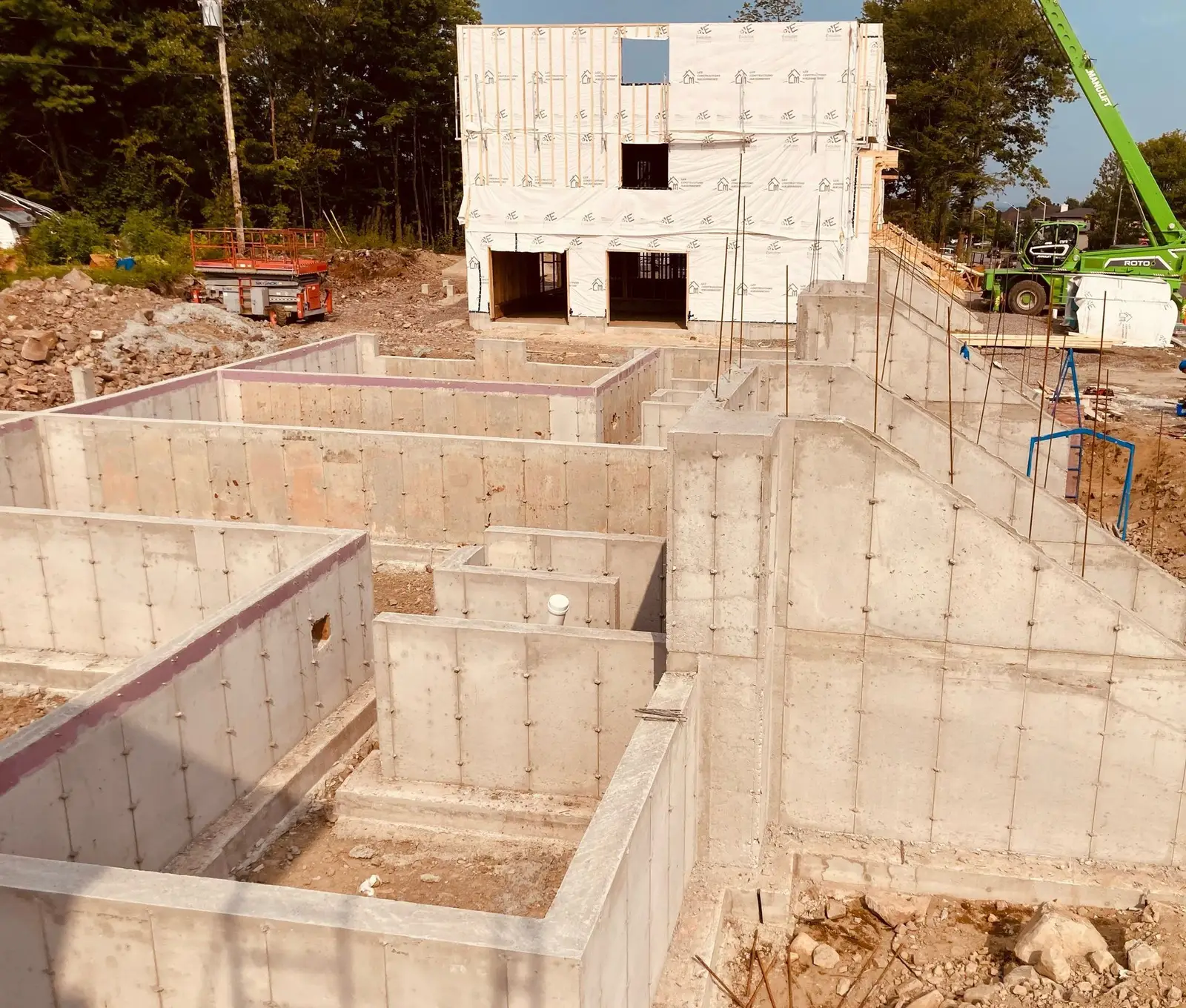 Fondation résidentielle décoffrée vue de haut, chaque pièce du sous-sol délimitée par ses murs de béton, bâtiment monté à l'arrière.
