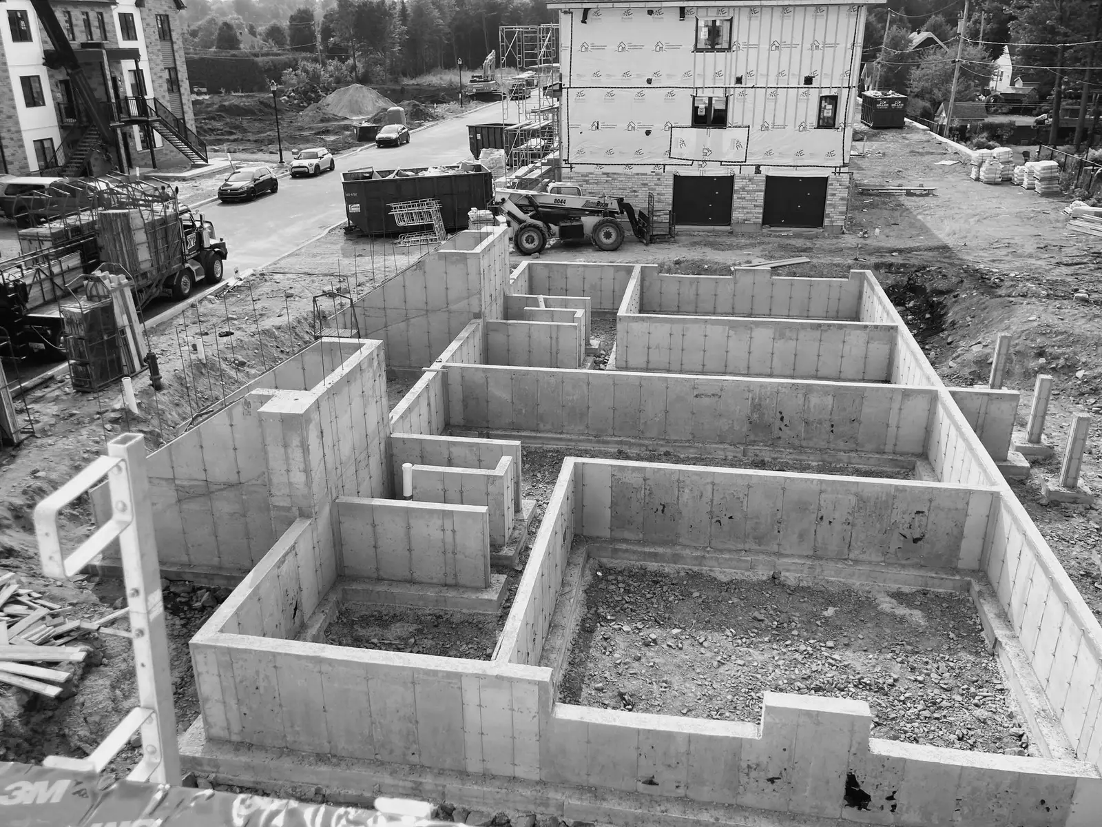 Photo noir et blanc d'une fondation décoffrée vue de haut, maison en construction et rue résidentielle à l'arrière-plan.