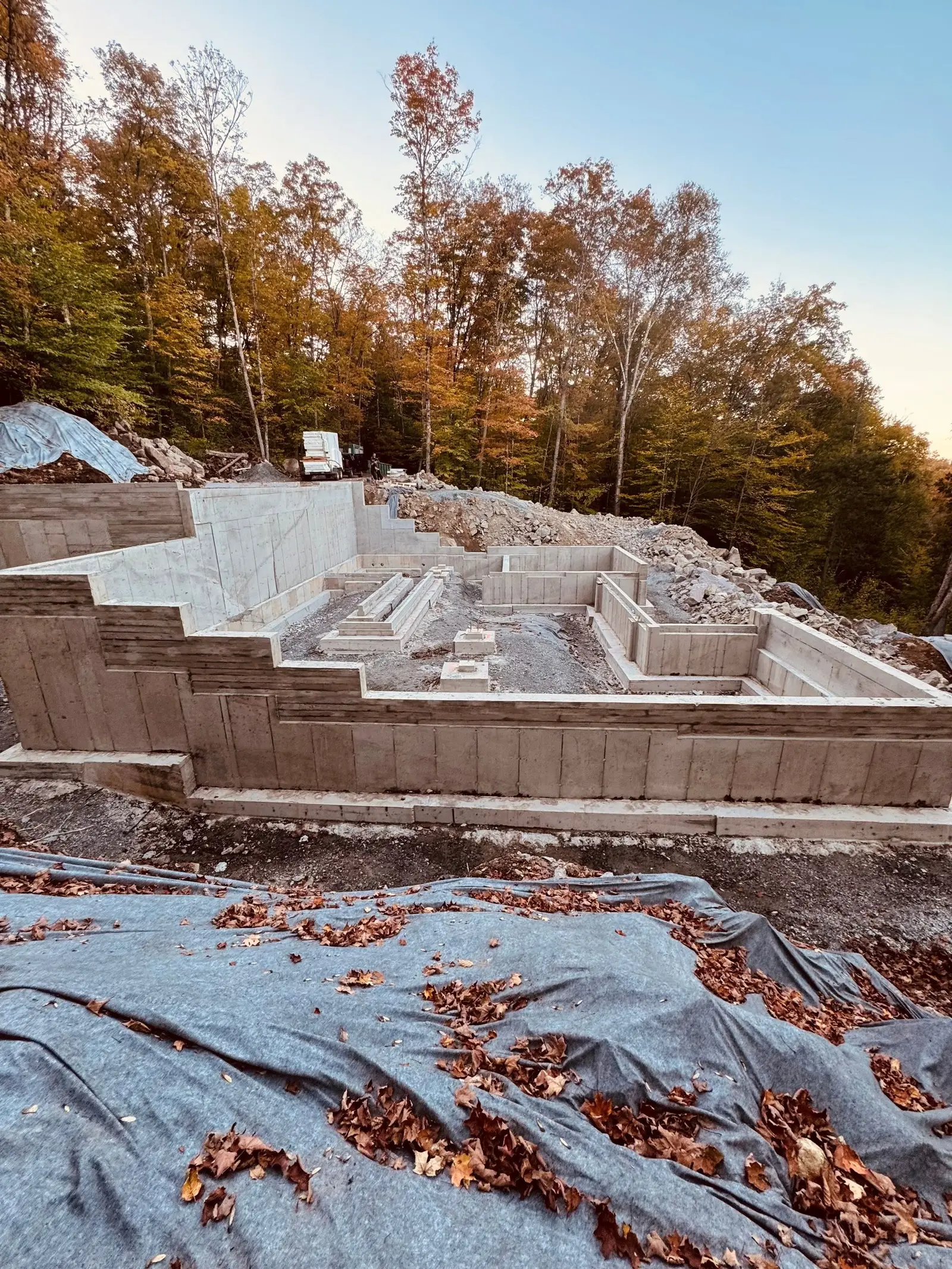 Fondation complète décoffrée en sous-bois : murs de béton apparents, paliers successifs et empattements dégagés.